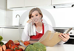 Young beautiful home cook woman in red apron at modern domestic kitchen reading cookbook following recipe