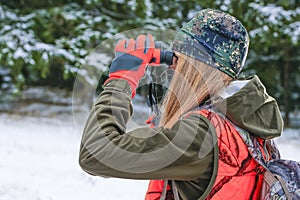 A young beautiful hunter woman looks into the binocular , looking for wild animals. She wear camouflage and hunting clothing