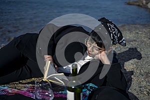 Young beautiful indian girl reading a book while leaning down on the ground wearing a black coat. Concept of having picnic in a