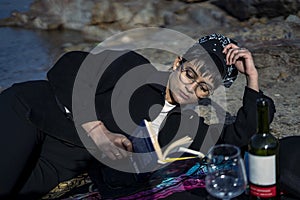 Young beautiful indian girl reading a book while leaning down on the ground wearing a black coat. Concept of having picnic in a