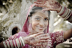 Young beautiful Indian Hindu bride standing under tree with painted hands raised