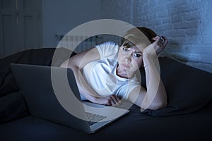 Young beautiful internet addicted sleepless and tired woman working on laptop in bed late at night