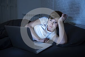 Young beautiful internet addicted sleepless and tired woman working on laptop in bed late at night