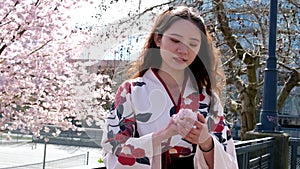 Young beautiful japanese girl wearing a traditional kimono acting to a camera under a cherry blossom tree in traditional