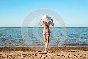 Young beautiful lady in hat with long hair walking along the beach.