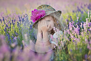 Young beautiful lady mother with lovely daughter walking on the lavender field on a weekend day in wonderful dresses and hats.