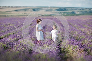 Young beautiful lady mother with lovely daughter walking on the lavender field on a weekend day in wonderful dresses and hats.