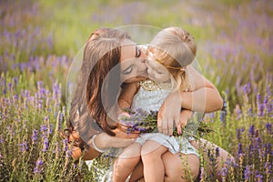 Young beautiful lady mother with lovely daughter walking on the lavender field on a weekend day in wonderful dresses and hats.