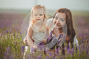 Young beautiful lady mother with lovely daughter walking on the lavender field on a weekend day in wonderful dresses and hats.