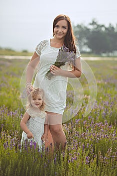 Young beautiful lady mother with lovely daughter walking on the lavender field on a weekend day in wonderful dresses and hats.