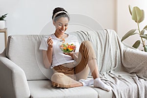 Young and beautiful lady sitting on couch, eating salad