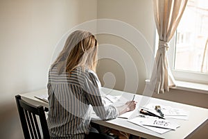 Young beautiful lady sitting at white desk and think about calligraphy