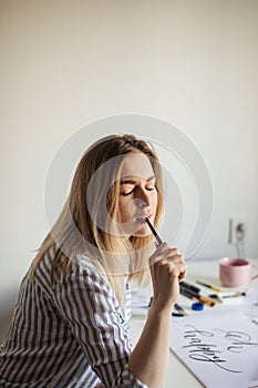 Young beautiful lady sitting at white desk and think about calligraphy