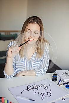 Young beautiful lady sitting at white desk and think about calligraphy