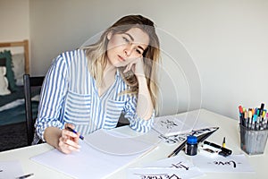 Young beautiful lady sitting at white desk and think about calligraphy