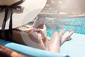 Young Beautiful lady wearing bikini using mobile phone sitting on chair in swimming pool