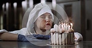 A young beautiful lady wearing blue gloves and a cookers uniform blows out the candles on the cake