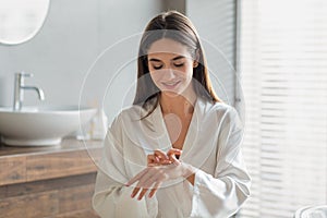 Young Beautiful Lady In White Silk Robe Applying Body Milk On Hands