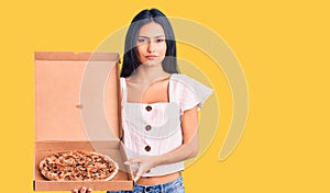 Young beautiful latin girl holding delivery pizza box thinking attitude and sober expression looking self confident