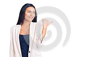 Young beautiful latin girl wearing business clothes smiling with happy face looking and pointing to the side with thumb up
