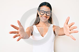 Young beautiful latin girl wearing casual clothes and glasses looking at the camera smiling with open arms for hug