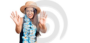 Young beautiful latin girl wearing hawaiian lei and summer hat afraid and terrified with fear expression stop gesture with hands,