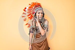 Young beautiful latin girl wearing indian costume hand on mouth telling secret rumor, whispering malicious talk conversation