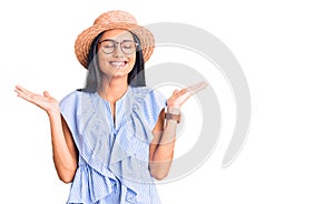 Young beautiful latin girl wearing summer hat and glasses celebrating mad and crazy for success with arms raised and closed eyes