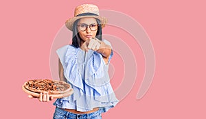 Young beautiful latin girl wearing summer hat and glasses holding pizza pointing with finger to the camera and to you, confident