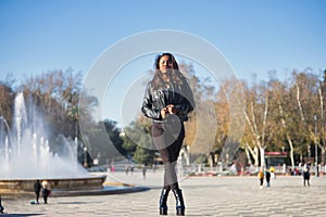 Young, beautiful, Latin and South American woman in leather jacket and top, jeans and platform shoes, clutching the lapels of the photo