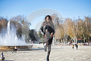 Young, beautiful, Latin and South American woman with leather jacket and top, jeans and platform shoes, hands in pockets posing