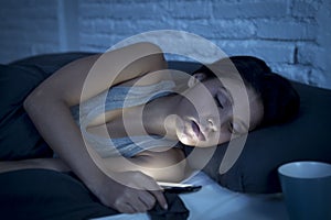 Young beautiful Latin woman on bed late at night texting using mobile phone tired falling sleep