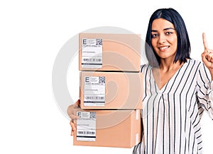 Young beautiful latin woman holding delivery package surprised with an idea or question pointing finger with happy face, number