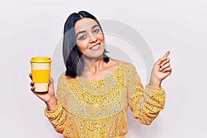 Young beautiful latin woman holding takeaway cup of coffee smiling happy pointing with hand and finger to the side