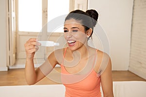 Young beautiful latin woman looking at pregnancy test feeling happy and excited at the positive result in bedroom at home. Materni