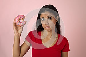 Young beautiful latin woman in red with pink sugar donut thinking and feeling guilty after biting