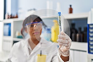 Young beautiful latin woman scientist looking test tube with plant at laboratory