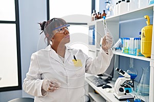 Young beautiful latin woman scientist looking test tube with plant at laboratory