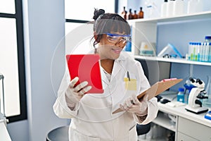 Young beautiful latin woman scientist using touchpad reading document at laboratory