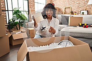 Young beautiful latin woman smiling confident unpacking cardboard box at new home