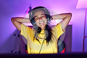 Young beautiful latin woman streamer smiling confident relaxed with hands on head at gaming room