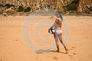 Young and beautiful latin woman with sunglasses is on the beach. The woman has her back turned and is holding a volleyball in her