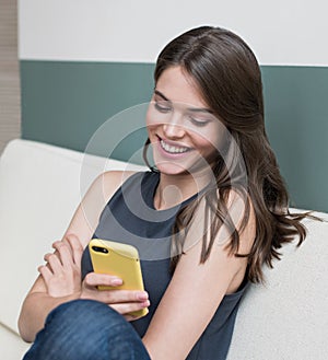 Young beautiful laughing woman using smart phone at home. Smiling girl texting on her phone