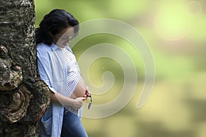 Young beautiful long haired brunette leaning on a bizarre tree and looking at her pregnant belly