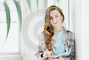 Young beautiful long haired college student girl in casual shirt with notebook, pen. Businesswoman making notes in