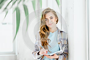 Young beautiful long haired college student girl in casual shirt with notebook, pen. Businesswoman making notes in