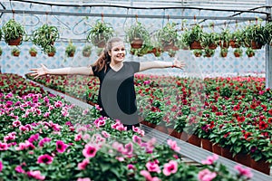 Young beautiful long-haired girl in a greenhouse with colorful flowers petunias in spring