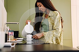 Young beautiful long-haired woman pouring hot water into a cup