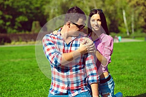 Young beautiful loving couple in checked shirts, jeans and sunglasses sitting on the green lawn