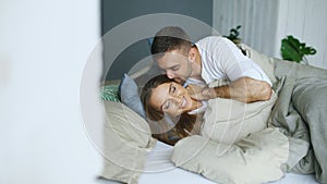 Young beautiful and loving couple wake up at the morning. Attractive man kiss and hug his wife in bed